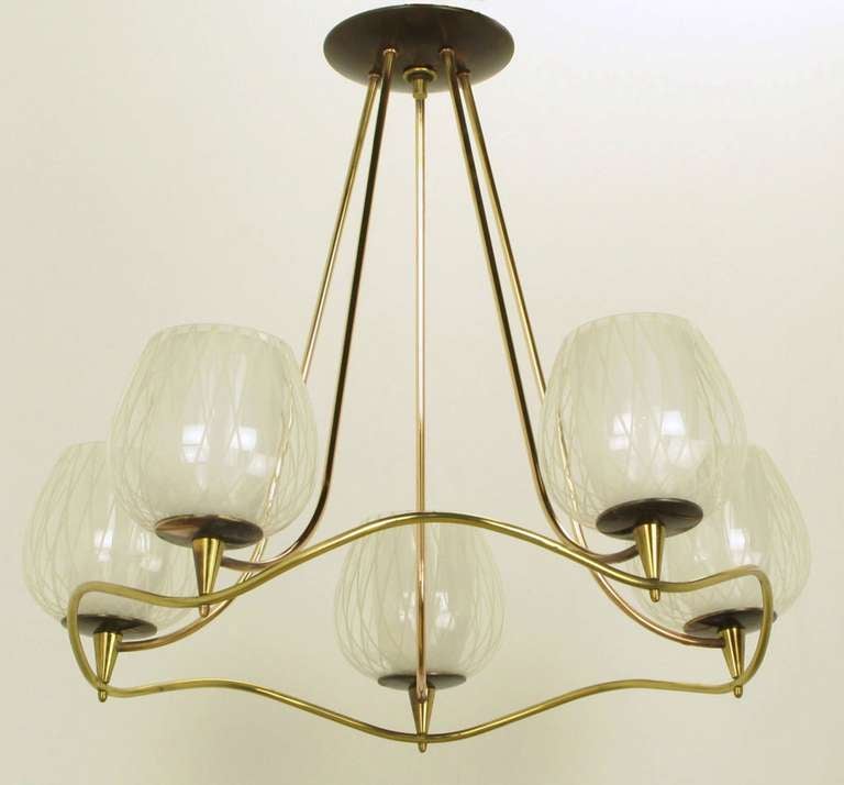 Very well designed chandelier of curvaceous brass rod and two-part etched and milk glass shades. Most likely by Gerald Thurston for Lightolier. Five two part shades consist of a milk glass interior hurricane surrounded by an etched wine glass clear