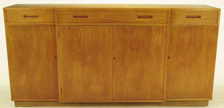 All original sideboard by Edward Wormley for Dunbar. Accentuated by figural wood grained top, carved and recessed drawer pulls, and brass sheathed key holes to the bottom cabinets. Plinth base wrapped in a brushed fawn colored leather.