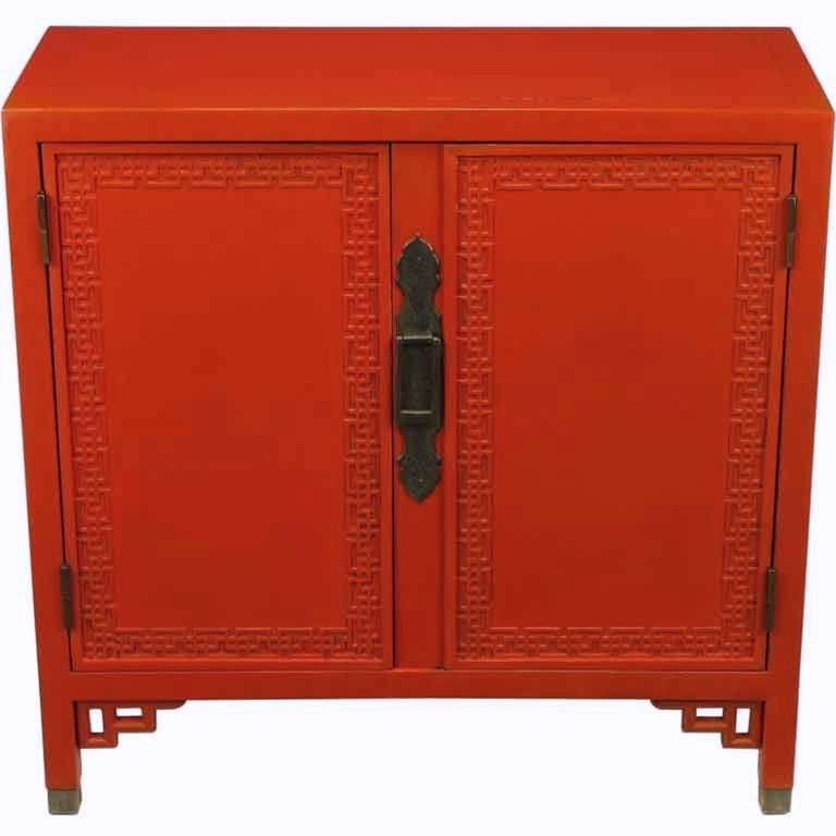 Cinnabar lacquer and black glazed two door Chinese Chippendale cabinet. Features a large patinated dragon etched brass strap escutcheon rectangular ring pull. Open fretwork bracketed legs with brass sabots. Two doors with closed fretwork borders