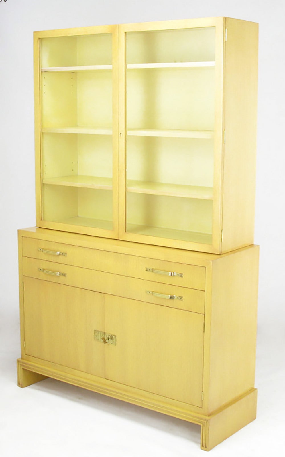 Restored two-piece China or display cabinet by Tommi Parzinger for Charak Modern. Bleached mahogany wood is finished in light saffron with a contrasting grain fill and glaze as was dictated by the original untouched finish behind the two cabinet