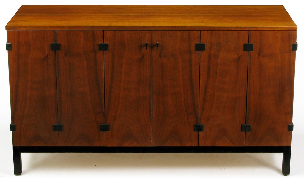 Sideboard with figured walnut tri-fold doors.  Exposed black lacquered metal hinges, and a black lacquer Parsons-style wood base, by Milo Baughman. Doors open to reveal three silverware and linen drawers, with five storage compartments. Manufactured