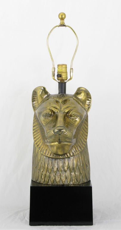 Heavy cast brass table lamp by Chapman, depicting the powerful mythological Egyptian warrior goddess, Sekhmet, who took the form of a lioness.  Black lacquered metal plinth block base and stem. Brass harp, socket and ball finial.