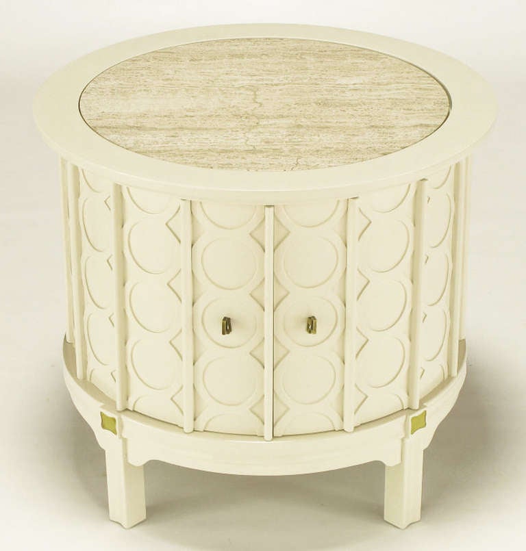 Restored pair of round travertine topped end tables in fresh bone white lacquer. Ribbed circular vertical relief detailing around entire circumference. Two front doors open via brass key pulls to reveal open storage. Brass inlay to the top of each