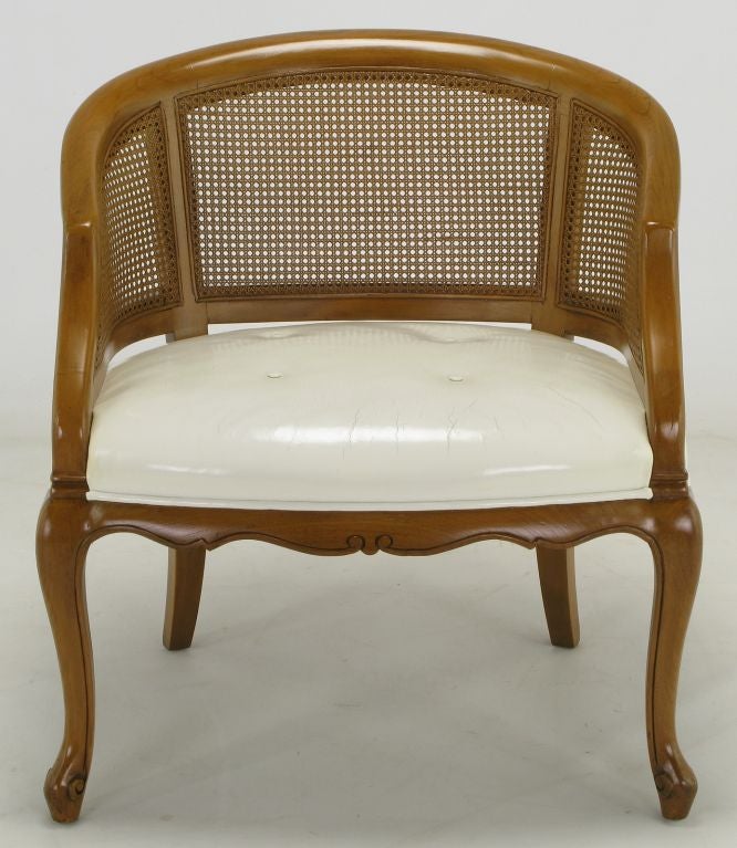 French regency cane back slope shoulder chair in walnut with a button tufted white leather seat. Slight and well placed carving on the cabriole front legs and the seat frame.