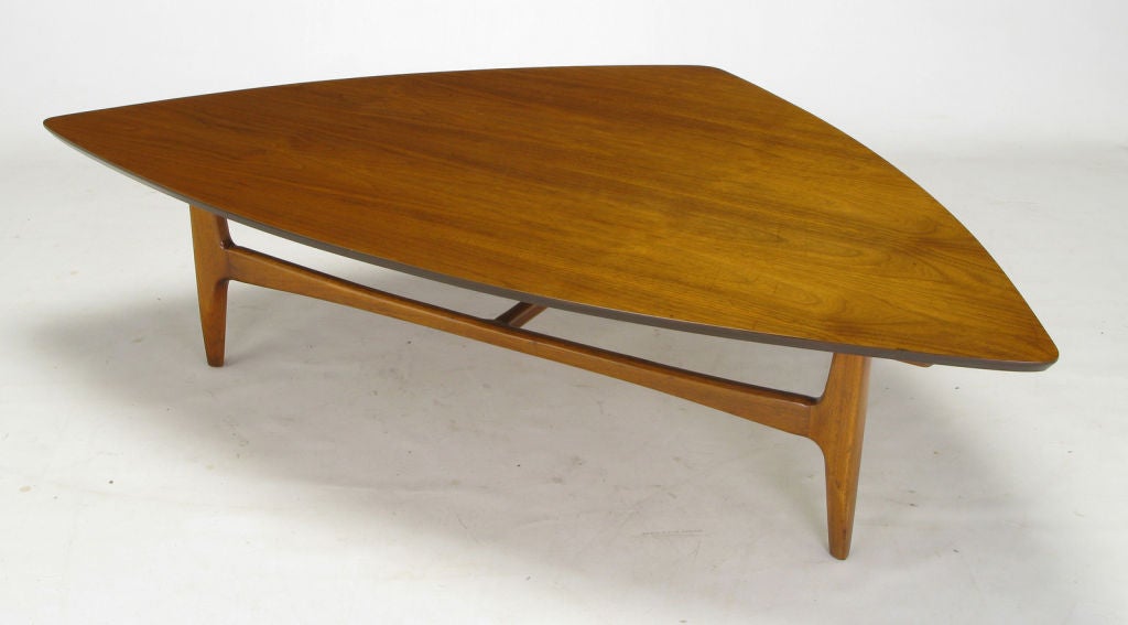 1950s modern walnut coffee table with a bowed isosceles triangular shaped top. The base is a three legged carved walnut design with a two part carved stretcher.