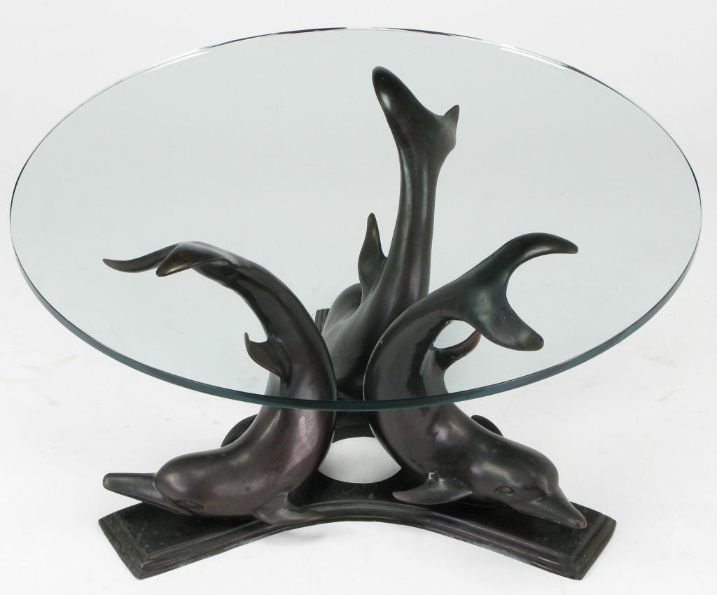 Cast Bronze coffee table comprised of three arched back dolphins arranged on a reverse trefoil aged bronze ogee edge base. Round glass top is 3/4