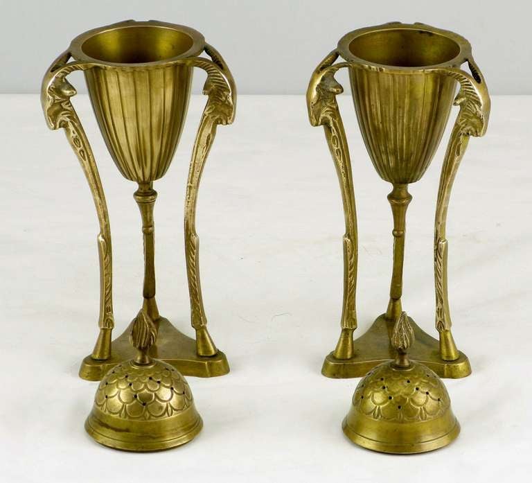 Urne in ottone in stile Impero splendidamente patinate, ornate da tre teste di ariete e gambe a pilastro scanalate sormontate da basi in ottone a trifoglio. Il tappo traforato è dotato di un terminale a fiamma ed è rimovibile. L'urna centrale conica
