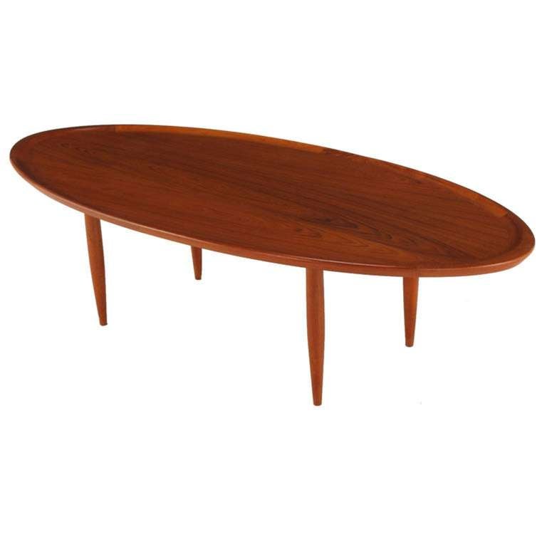 Clean lined oval teak wood coffee table with simple tapered legs and a rich wood grain. The sculpted oval top is incised lending the visual appearance of a tray.