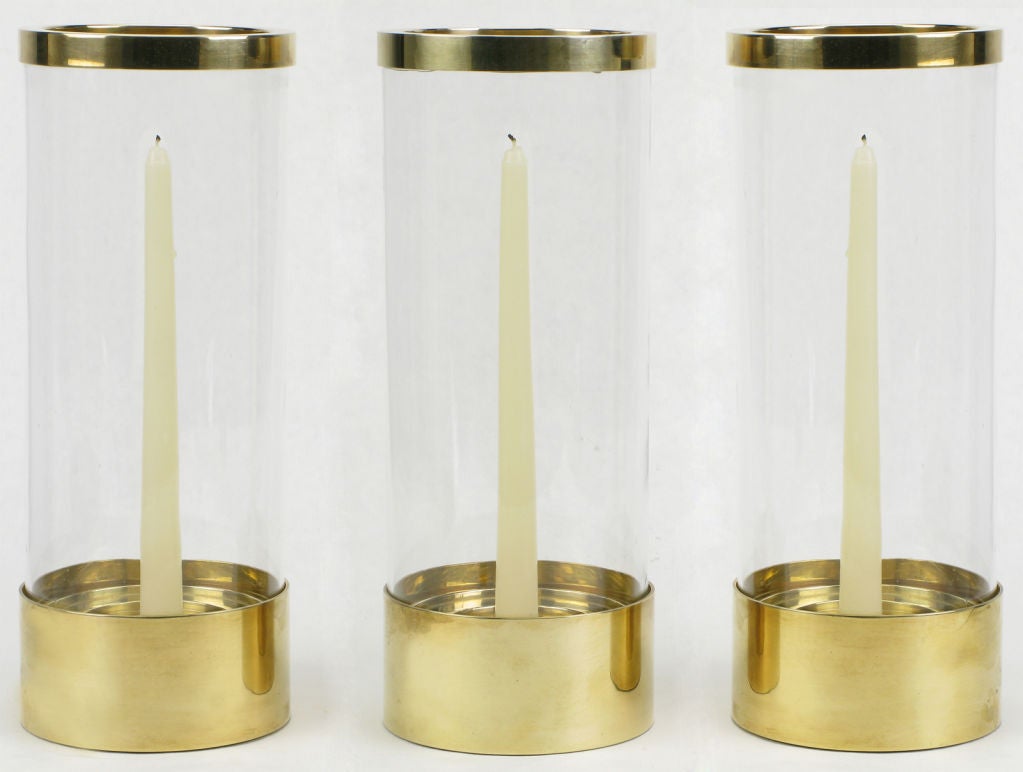 Chapman Lighting, brass and clear hand blown glass hurricane shade candle holders with brass rimmed top and heavily cast brass graduated base to fit a variety of candle sizes. Sold as a set of three.