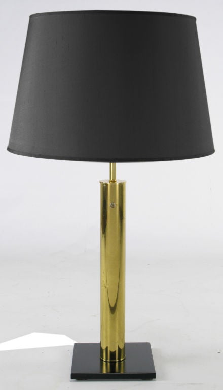 Brass cylinder table lamp with black lacquered steel base by Walter Von Nessen for Nessen Lighting. Brass stem and factory issued articulated white porcelain sockets and white lacquered housing.