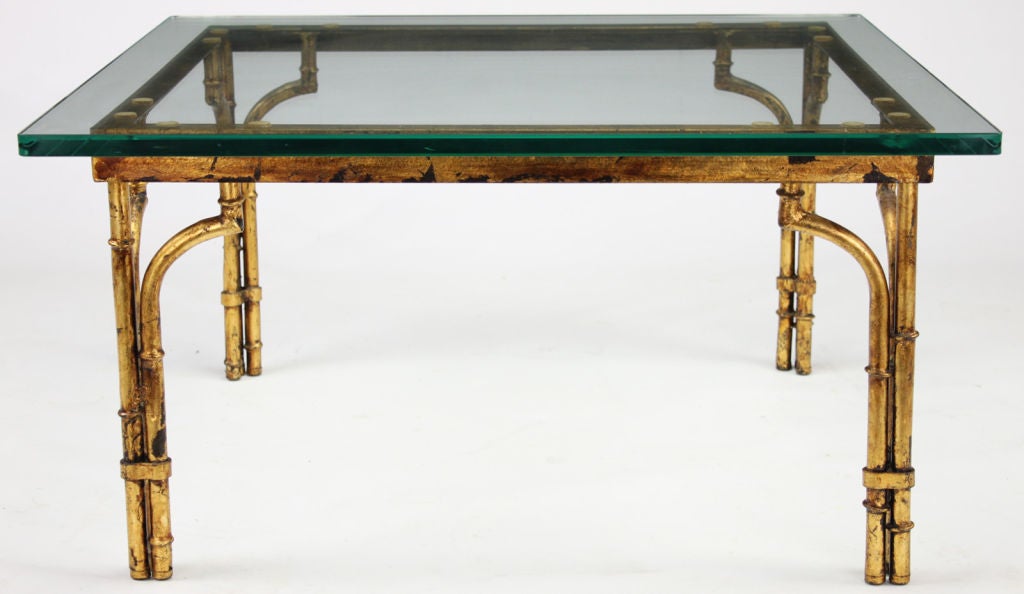 Table basse en métal de forme bambou en finition feuille d'or vieilli avec plateau en verre carré. Chaque pied est constitué de colonnes reliées en trois parties, la colonne extérieure étant terminée par des équerres d'angle.