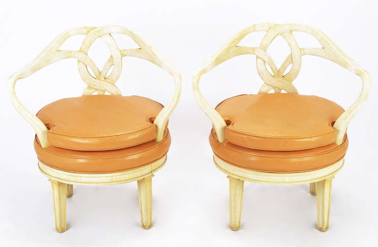 Striking and sculptural pair of Italian Empire style swiveling armchairs. Round seats and sinuous arms that intertwine to form the back. Frames are finished in a cream lacquer under a saffron glaze. Seats are upholstered in pumpkin color leather.