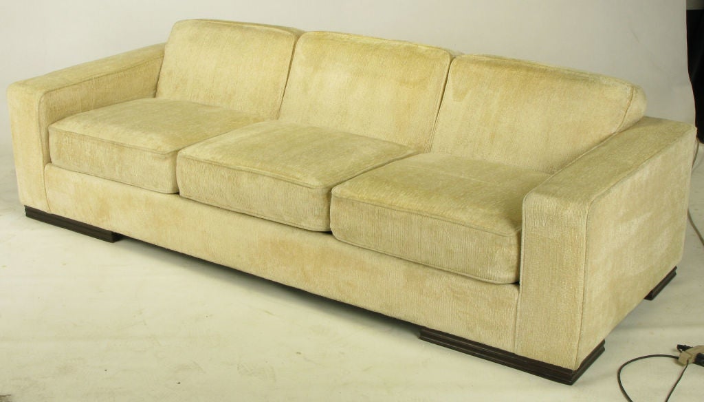 Larry Laslo for John Widdicomb art deco revival sofa in cream textured chenille with wide low arms, thick loose cushioned seats and a canted fixed three part back. Four long carved wood feet.