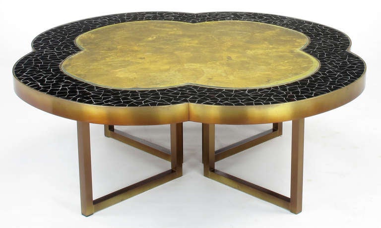 Custom designed coffee table with four square profile lacquered brass legs and brass bordered quatrefoil top. Top surface is comprised of black glass mosaic with glass covered gold leafed center. Some pieces of the black glass have red highlights.