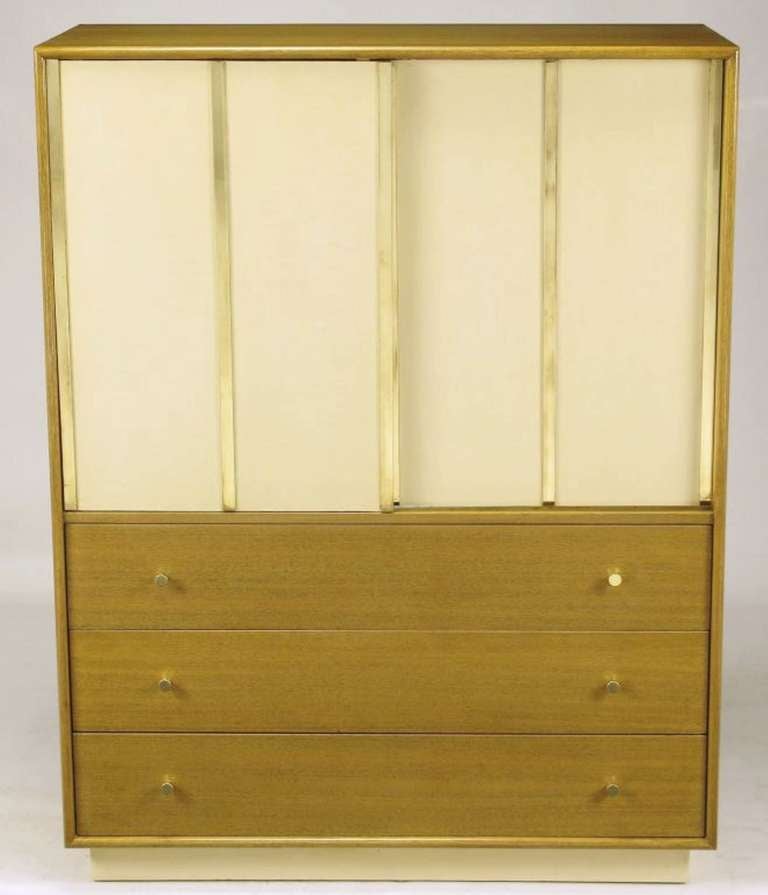 Harvey Probber bleached mahogany tall dresser or gentleman's chest, with ivory leather-clad sliding doors that feature brass flat bar appointments. Behind the doors there are four drawers and three sliding shelves. Three lower drawers open via