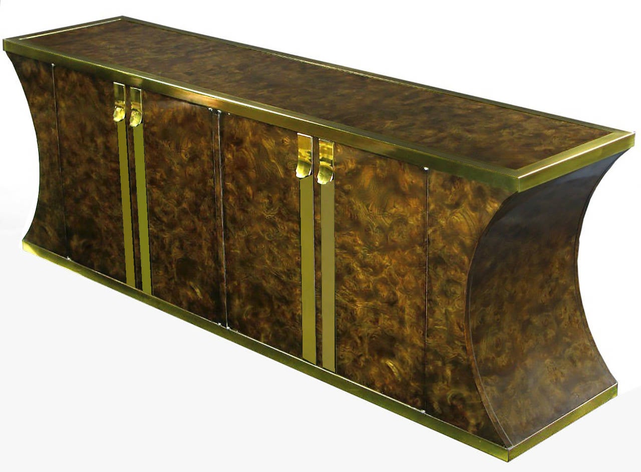 Mastercraft sideboard clad in vibrant Amboyna burl veneer, with heavy brass appointments. It is quite striking, with its inverted curve ends. Four drawers on one side, and shelf storage on the other.