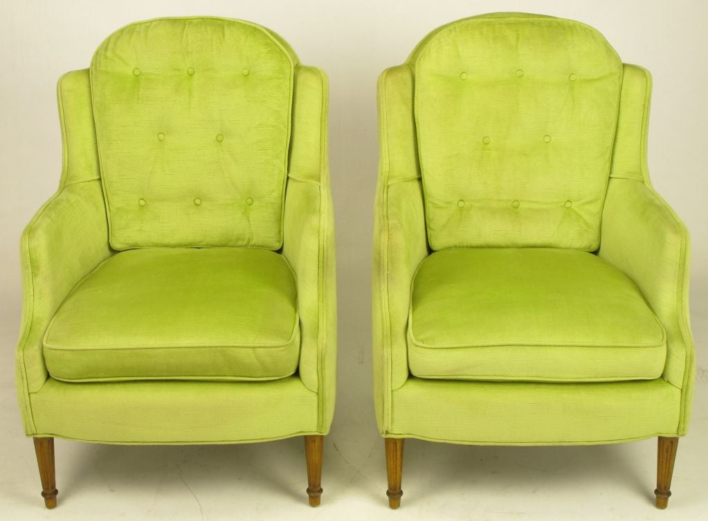 Elegant and comfortable chartreuse silk velvet regency lounge chairs. Tall arch top backs with fixed button tufted cushions, slight wings and loose cushion seat. Fluted walnut front legs with tapered walnut back legs.
