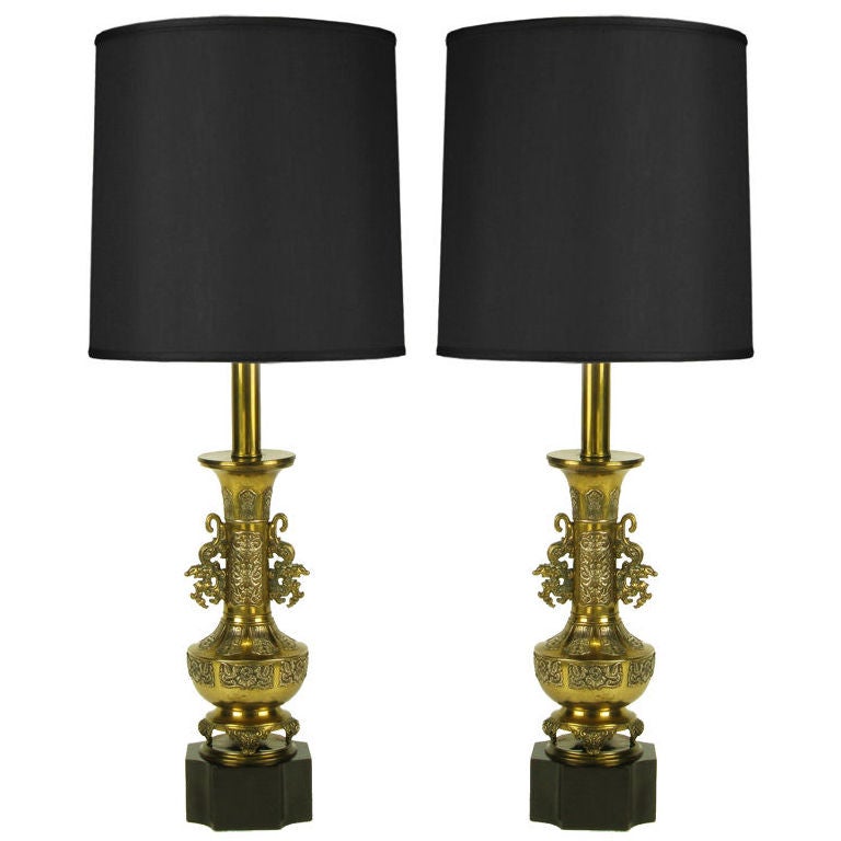 Cast brass footed urn form Chinese table lamp with traditional ceremonial dragon handles. Detailed with Asian flora and fauna and surmounted on a black lacquered reverse quatrefoil tall wood base. Dual brass socket illumination and adjustable brass
