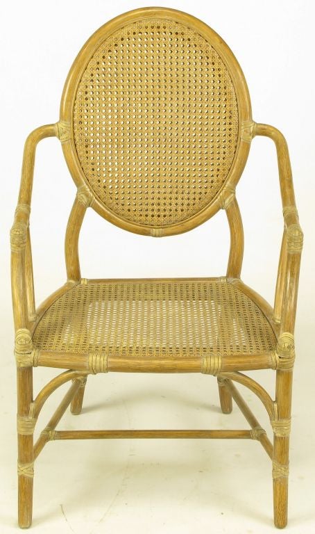 Set of six Louis XVI inspired limed rattan and cane armed dining chairs by McGuire of San Francisco. Double caned oval back with support coming from the arms as well as the legs. Rawhide strips bind all joints, adding superior strength. Slight flare