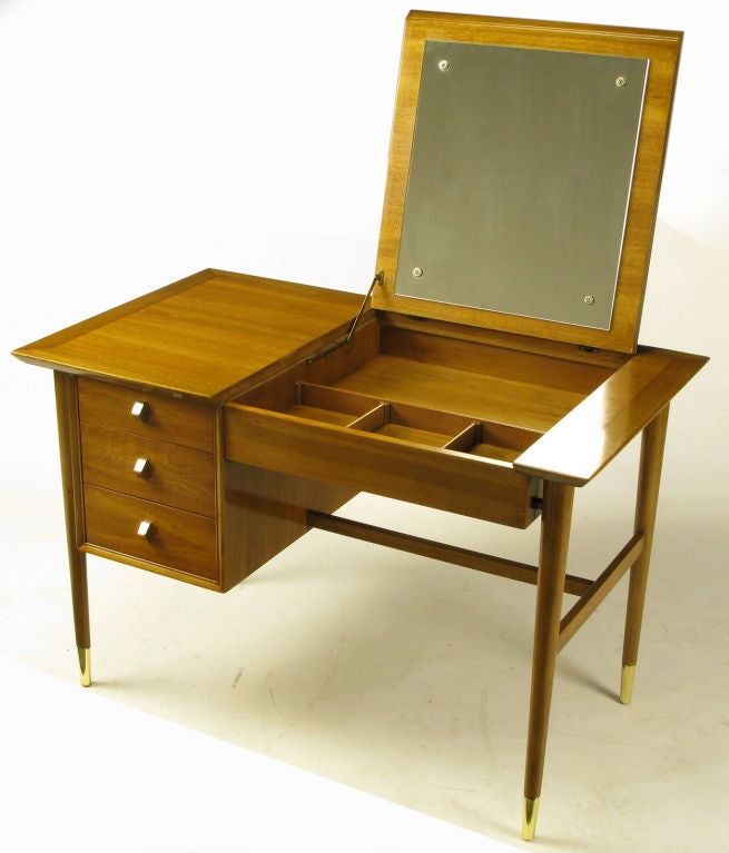 Beautifully designed flip top vanity/desk by Landstrom Furniture. Mahogany tapered dowel legs finish at polished brass sabots. They connect to the three drawer case and front apron via mahogany spacers giving the appearance of a floating piece. <br