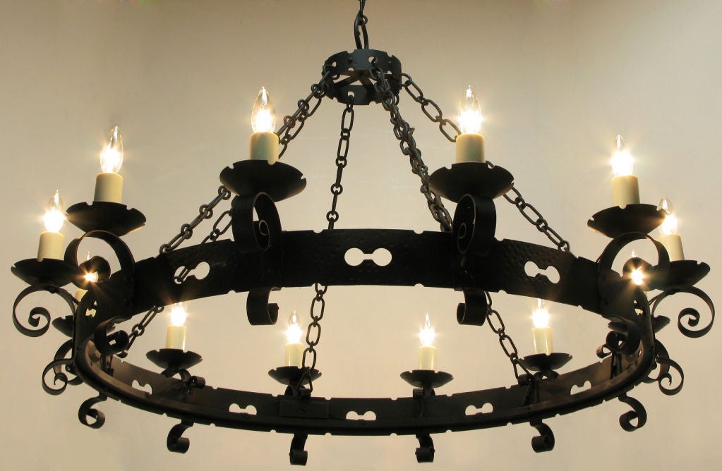 Rare Lightolier Spanish Revival twelve light black wrought iron chandelier. Large pierced and hammered ring with scrolled arms and notched bobeches. Six heavy round and oval link stands of chain meet at another small hammered and pierced ring.