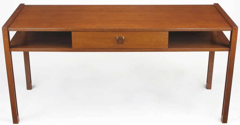 Edward Wormley for Dunbar console table in walnut with two levels supported by Parsons style legs subtly accented by inset reveals. Single center drawer, carved rosewood drop pull supported by brass squares with internal brass pivot. Understated
