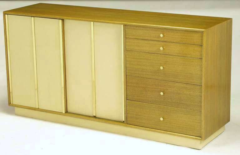 Harvey Probber bleached mahogany long dresser with ivory leather-clad sliding doors and plinth base. Three brass flat bars detail each leather door, giving the appearance of four sections. Behind sliding doors are four additional drawers and three