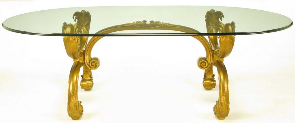Elegant Regency-inspired cast and gilt aluminum X-base ding table. Arched stretcher with center foliate detail and scrolled ends. Race track oval glass top with a beveled ogee edge.