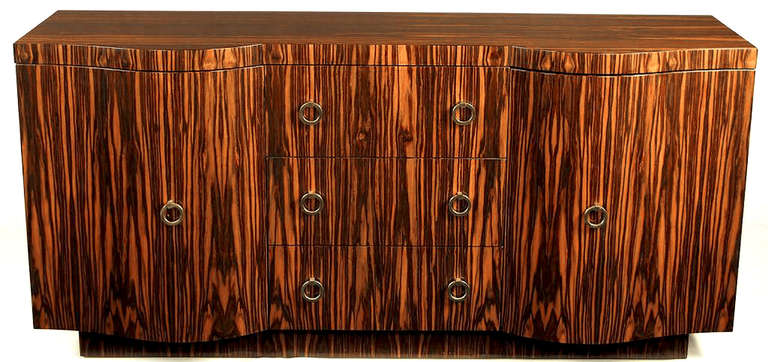 Vintage Interior Crafts sideboard with open hutch top has serpentine front doors that bookend three drawers. Entire exterior is veneered in macassar ebony with brass drop ring pulls. Can be used as a sideboard with the unattached top. Measurements