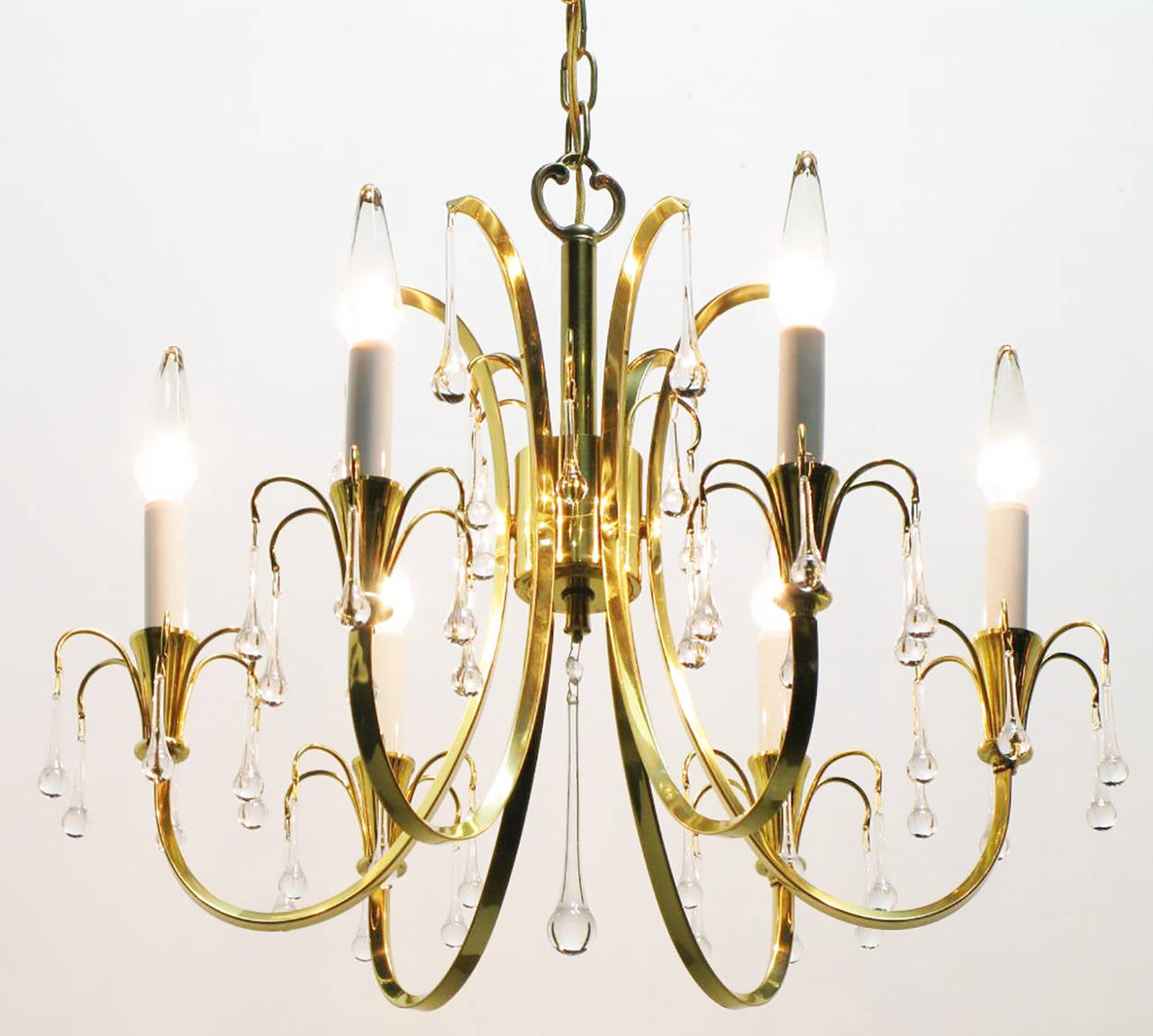 Modernist crystal chandelier with six C-curve arms and brass end cups. Raindrop crystals hang from every arm, with long center teardrop crystal. Sold with decorative chain and canopy.