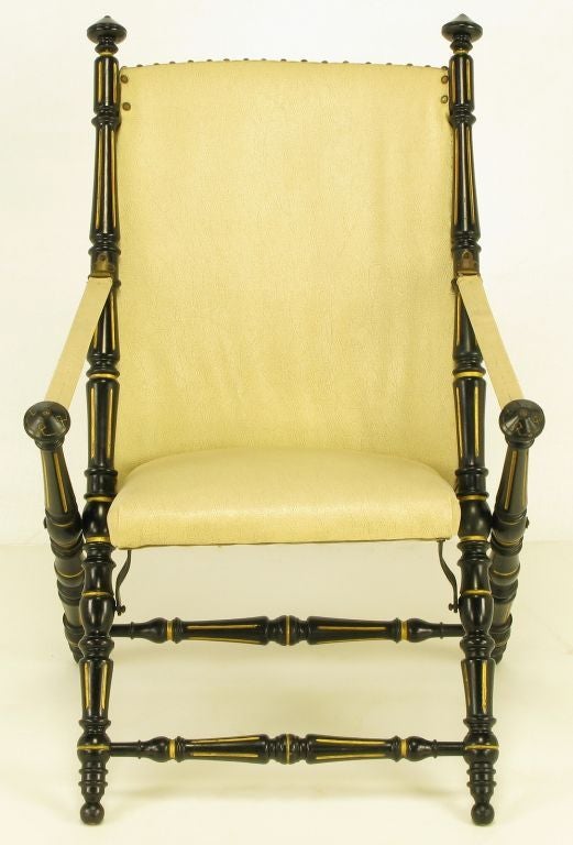 Heavily carved wood English style campaign chair finished in black lacquer and parcel gilt detailing. Ivory vinyl upholstered seat and back with brass nail heads. Plywood backed seat with metal supports.
