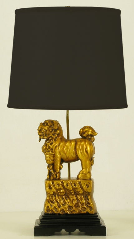 Gilt plaster food dog statue on gilt styled rock formation base  table lamp with stepped and ebonized carved wood base. Brass stem and socket mounted to the back of the statue at the carved wood base. Sold sans shade.