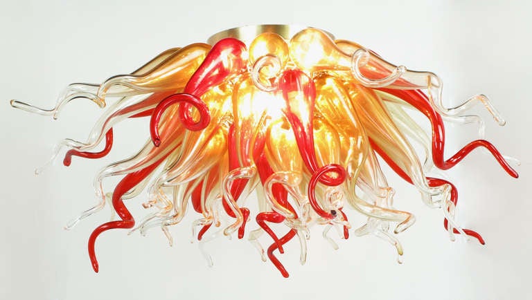 Sculptural handblown crimson and gold glass chandelier. Measure 42" in diameter and consisting of 54 spiral gourd shaped individual pieces. Mounted easily to the ceiling via a brushed brass and brass toned steel bracketed eight light