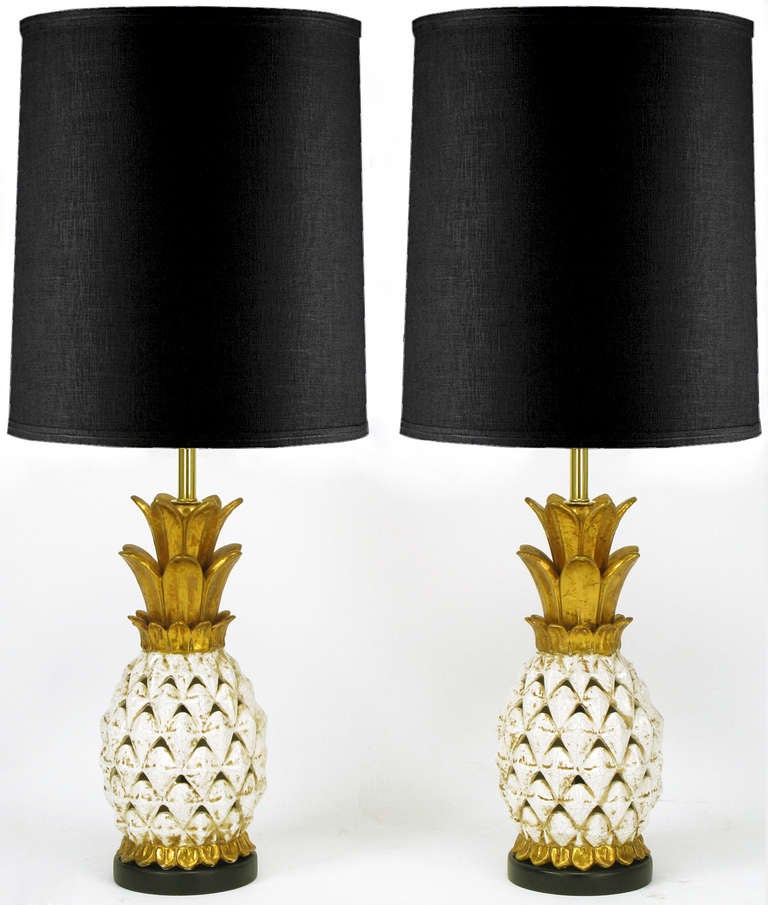 Pair of pierced ceramic body table lamps in the shape of white glazed and parcel gilt pineapples with gilt crown. Black lacquered wood base, brass stems, and double sockets with ball end pull chain.