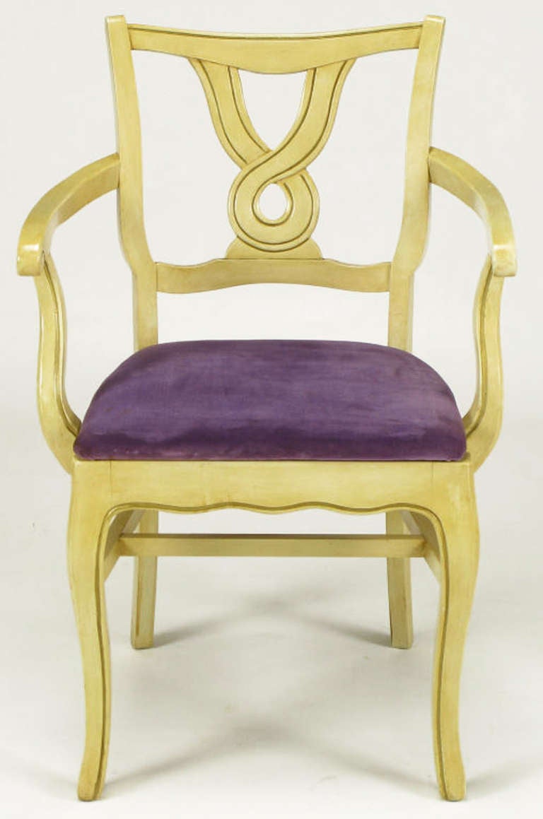 Uncommon set of six regency style dining armchairs with ivory glazed and parcel gilt carved wood frames with amethyst velvet seats. Cabriole front legs with scalloped aprons and high stretchers. Backs are a unique crossed ribbon open circle carving.