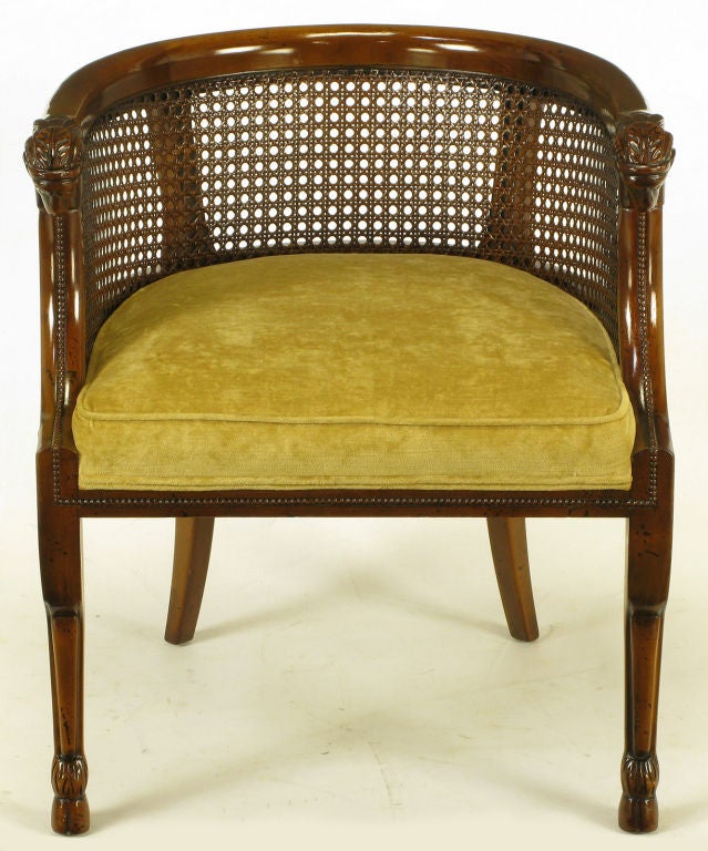 Empire style barrel back arm chairs. Each chair has a pair of hand carved ram's heads at the peak of the front legs which are dramatically shaped similar to actual ram hind legs with hooves as feet. Original gold velvet upholstery and caned back and