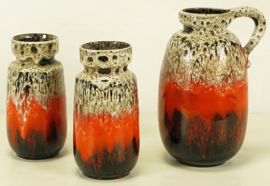 Set of three lava glazed ceramic vessels including a single handle pitcher or vase and a pair of recessed lipped vases. Colorful red, brown/black and heathered taupe glazing. Manufactured by Blue Mountain Pottery. Similar in appearance to postwar