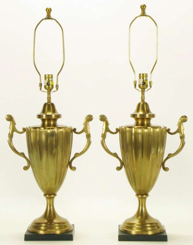 Pair heavy solid brass urn form table lamps by Chapman Lighting. Stepped trumpeted bases on honed black stone plinths. Reeded bodies with sinuous handles.