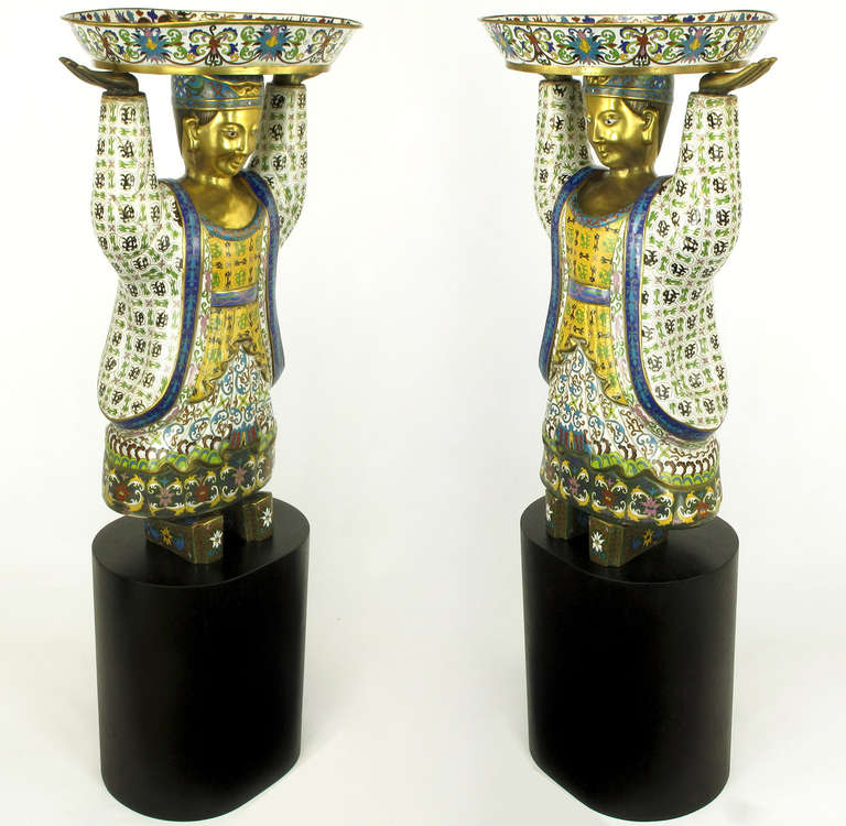 Stunning in presentation, these cloisonne figures depict finely robed men bearing bowl-like vessels overhead. Beautifully enameled in white, black, blue, red, green and gold. Faces and hands look to be gilt over brass or bronze.

Mounted as