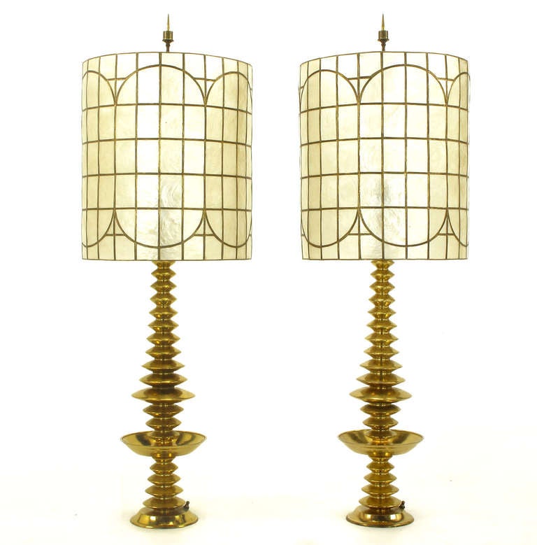 Pair of stacked saucer Art Deco or Machine Age spun solid brass table lamps with matching capiz shell shades. Concentric discs ascend and descend with large bobeches. Bowl shaped base with switch. In the manner of James Mont.