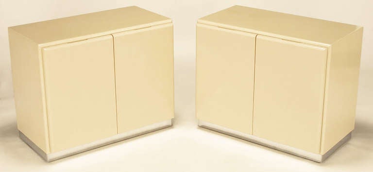 Pair of clean lined two-door cabinets in ivory lacquer on chromed metal over wood bases by Milo Baughman for Thayer Coggin. Two doors open to reveal a single shelf in each cabinet. Would make simple, yet elegant, nightstands. Also comes with a