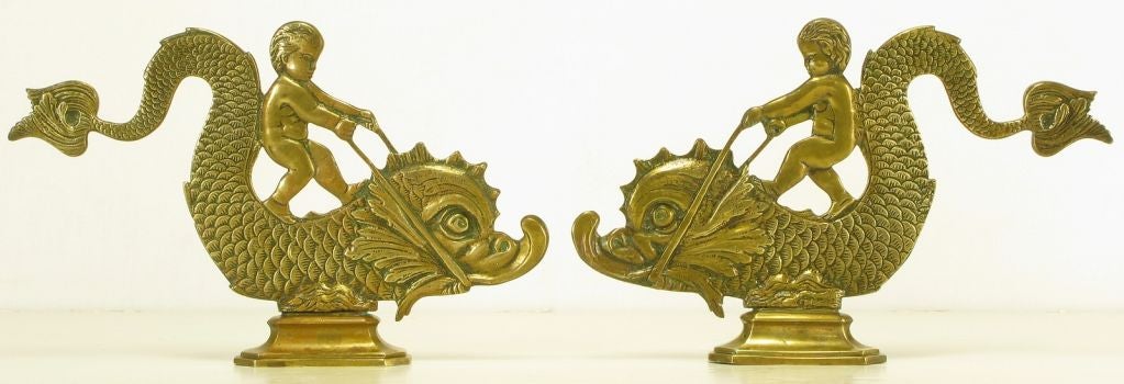 Pair of cast brass double-sided table or shelf ornaments of cherubs riding dolphins. Could also be used as fireplace andirons.