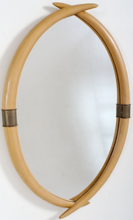 Vintage Chapman at its best. Four faux elephant tusks crossed at top and bottom frame the mirror, with brass ferrules and banding in the middle.