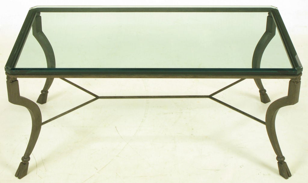 Antiqued metal hand wrought and welded iron coffee table with canted legs and hoofed feet with iron ball spacers. Double Y stretcher support and beveled glass top with canted corners.