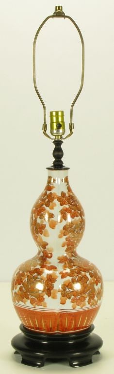 Double gourd form ceramic hand painted and parcel gilt Asian inspired table lamp with footed black lacquered carved and stepped wood base. Persimmon colored peony flowers and foliage outlined in gilt detail.