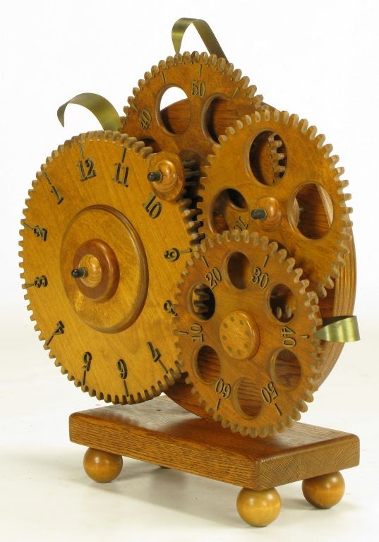 Uncommon wood gear desk clock mounted on oak wood base with carved oak ball feet. Electric clock mechanism with brass pointers/fixed hands. As the gears rotate the time advances. Seconds move the quickest followed by minutes and lastly hours. The