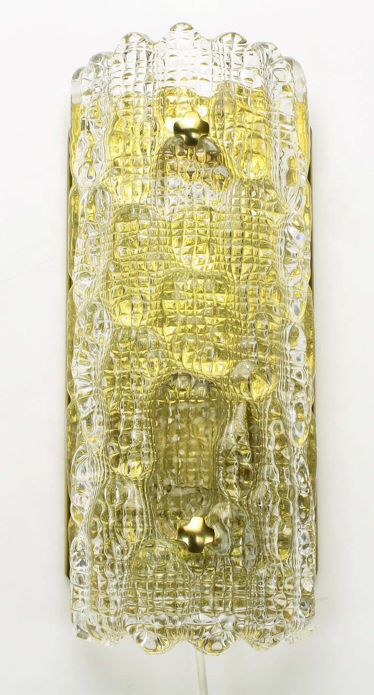 Paire d'appliques Carl Fagerlund pour Orrefors en verre texturé et courbé et en laiton. Chaque applique a une puissance maximale de 25 watts et peut être fixée au mur ou facilement montée à l'aide de vis et branchée dans une prise murale à l'aide du
