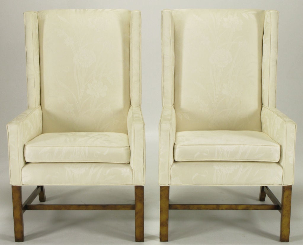 Pair of clean lined wing back chairs upholstered in a cream silk damask with oil drop lacquered wood legs and stretchers resembling a tortoise shell finish. Possibly a Henredon design, as they were the head chairs to a Henredon dining set.