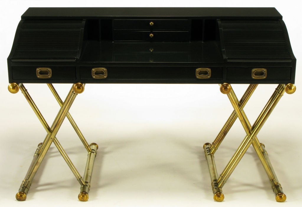 Black lacquered rolltop desk with pair of center top drawers, and compartmented openings behind tambour side sections. Three lower drawers. Brass campaign style pulls and side handles. Double x-form wood bases in aged silver leaf with gold leaf