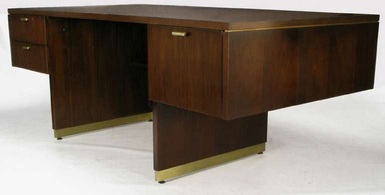 Uncommon modern executive desk by venerable American desk manufacturer, Myrtle Desk Co. Walnut body is on an open pedestal base, with a recessed shelf, and brass inlay. The three drawers have pulls that are solid brass halved bars, with nice patina